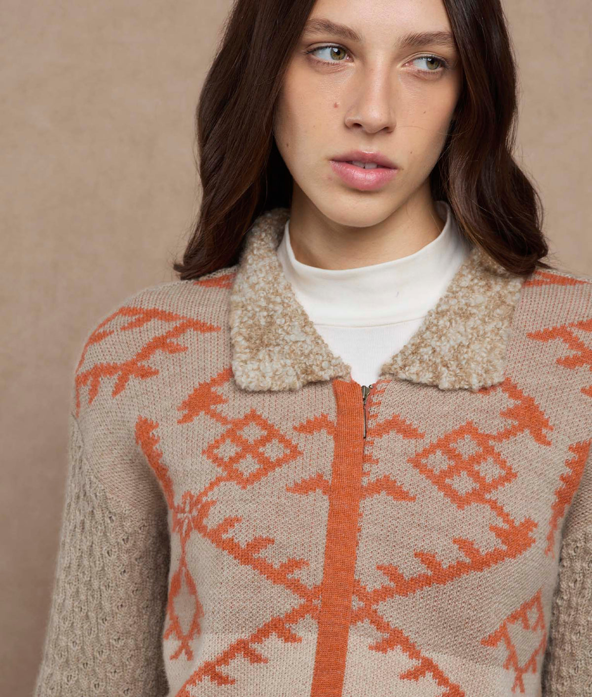 Close-up of a beige zip-up knit cardigan with an orange geometric pattern and textured collar.