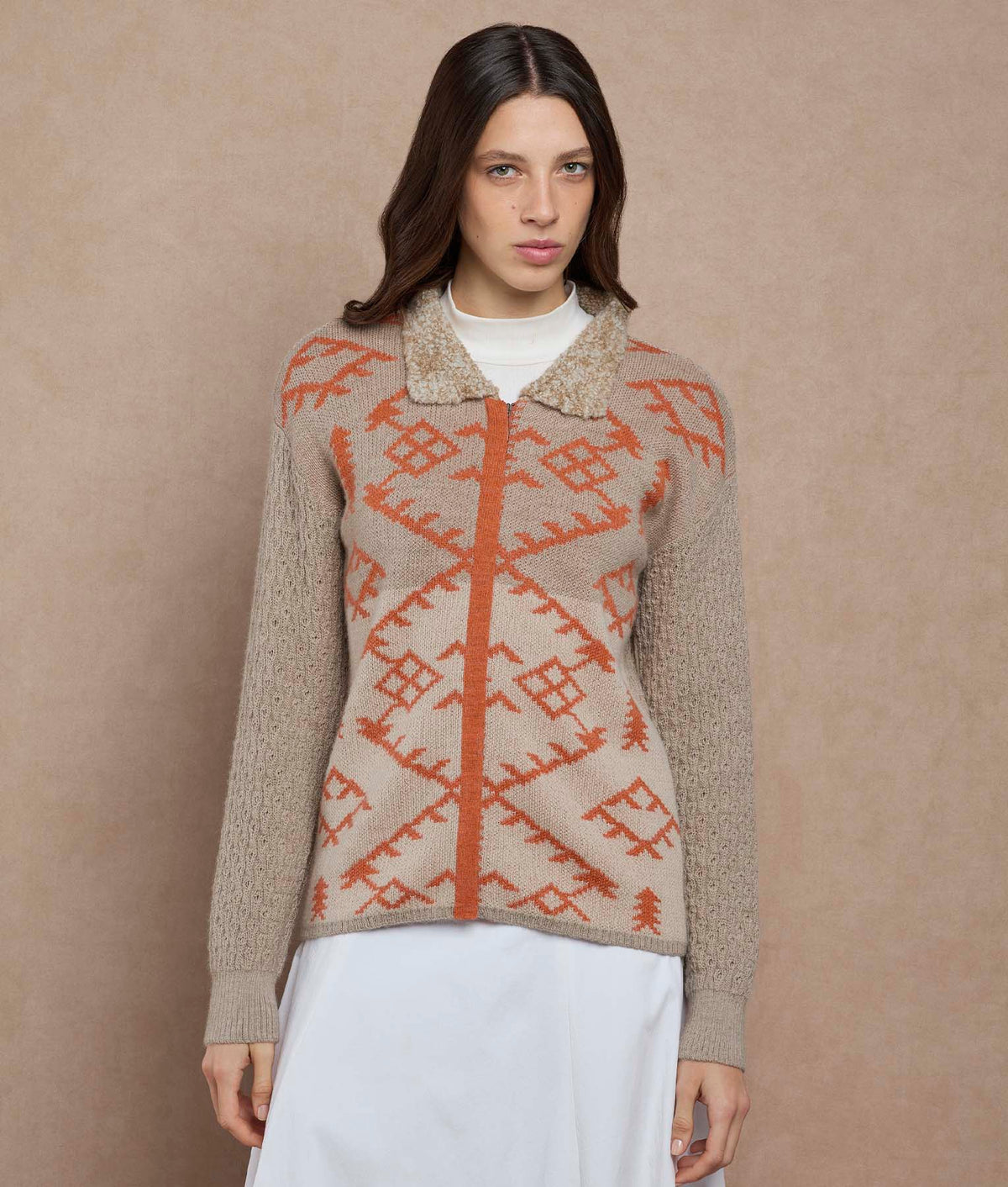 Woman wearing a beige knit cardigan with a rust-orange geometric pattern and textured collar.