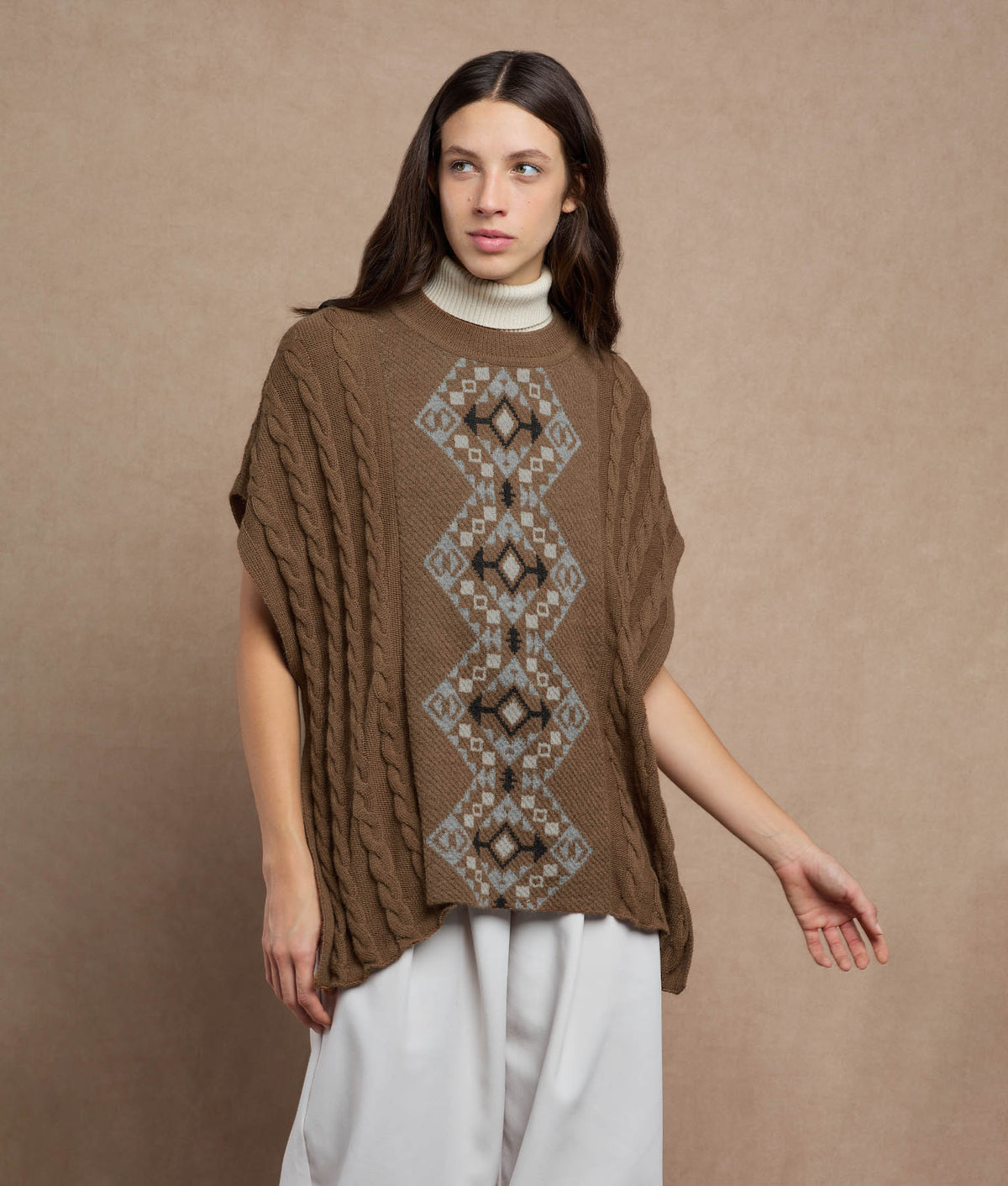 Woman wearing a brown knit poncho with a central geometric pattern.