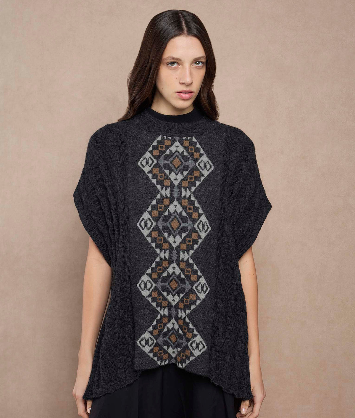 Woman wearing a black knit poncho with a gray, white and brown geometric diamond pattern.