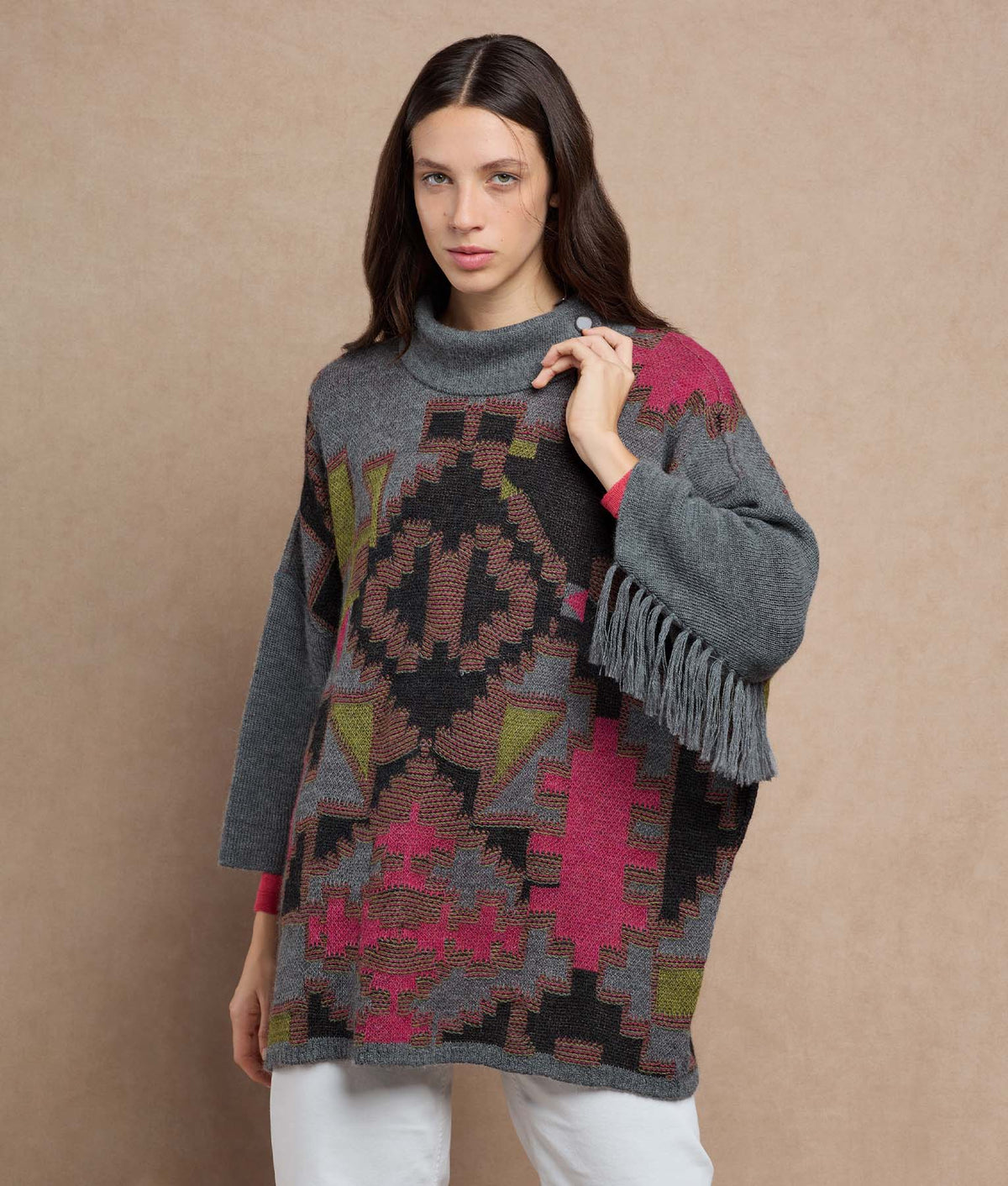 Woman wearing a gray knit poncho with a colorful geometric pattern and fringe.