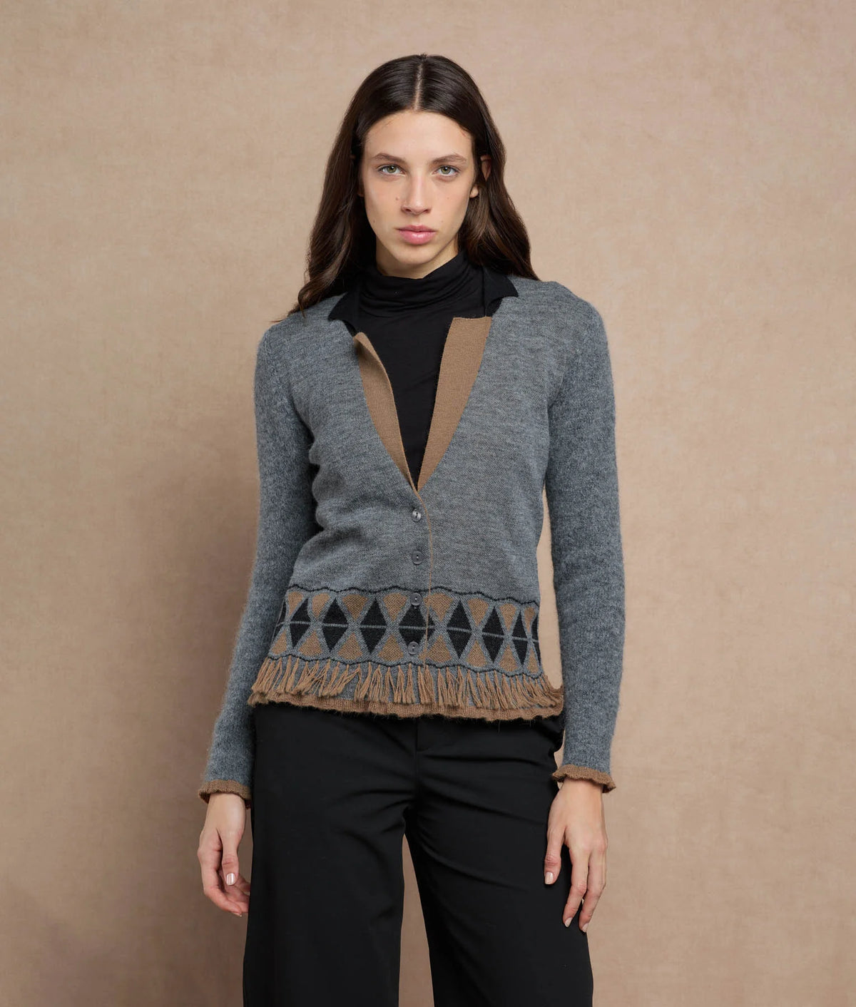 Woman wearing a gray knit cardigan with a brown geometric pattern and fringe trim.