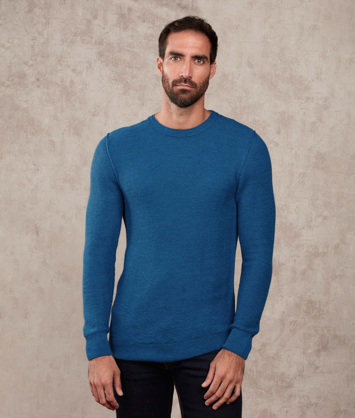 Man wearing a heathered medium blue crewneck sweater.