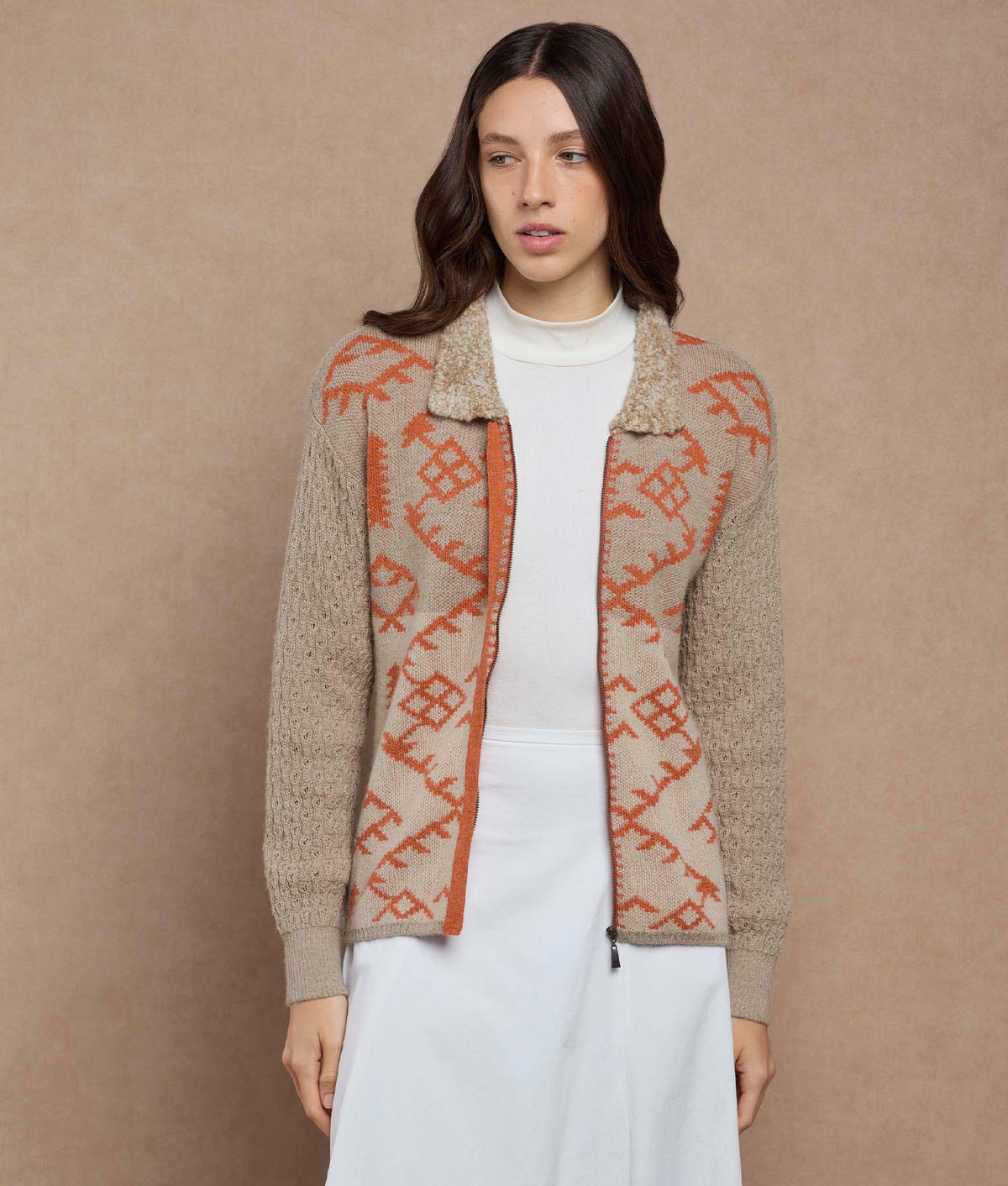 Woman wearing a beige zip-front knit cardigan with orange geometric patterns and a textured collar.