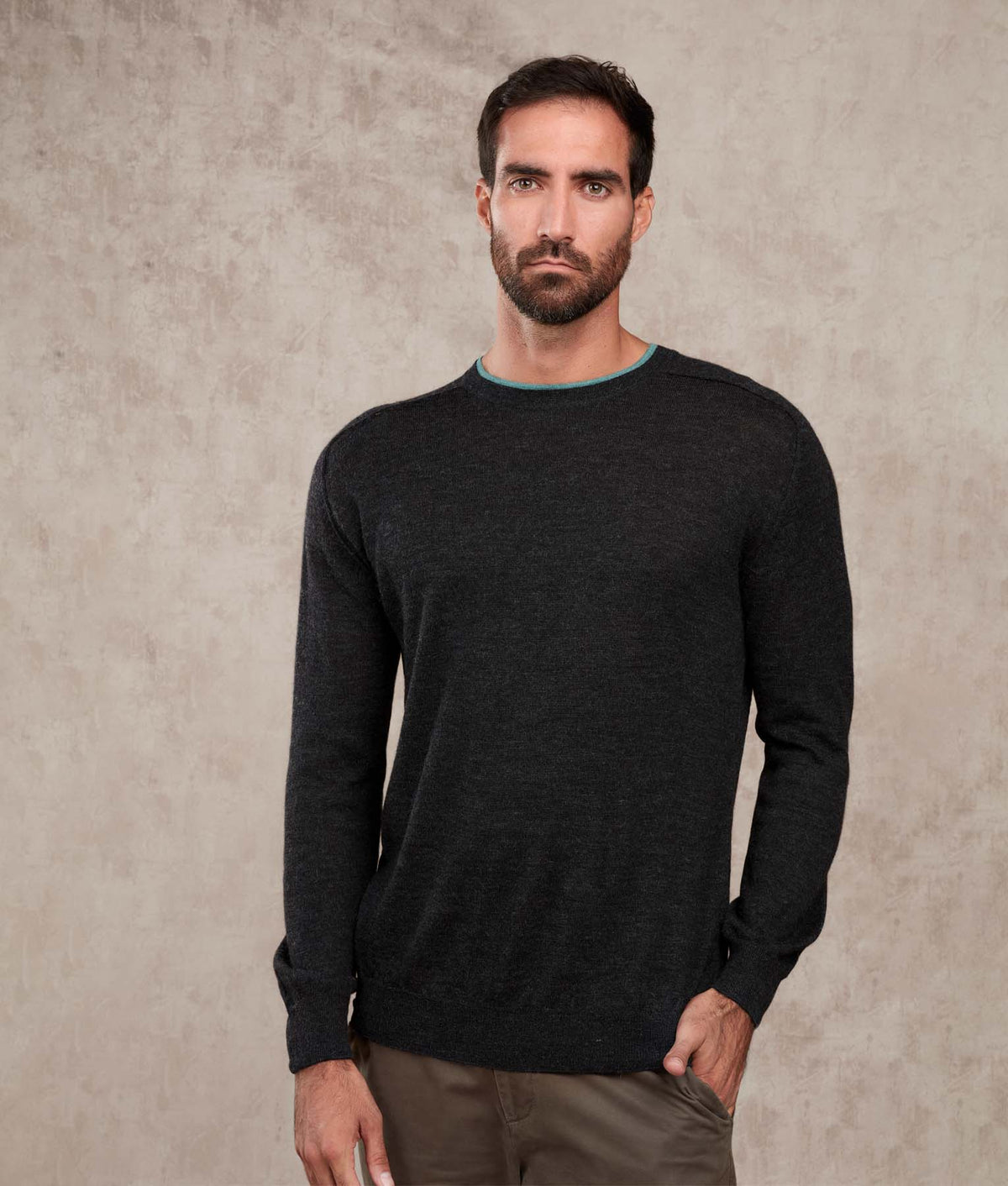 Man wearing a dark charcoal gray crewneck sweater with light blue-green collar trim.