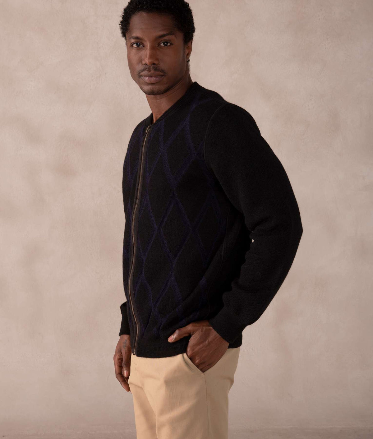 Man wearing a black zip-up knit sweater with a dark navy argyle pattern.