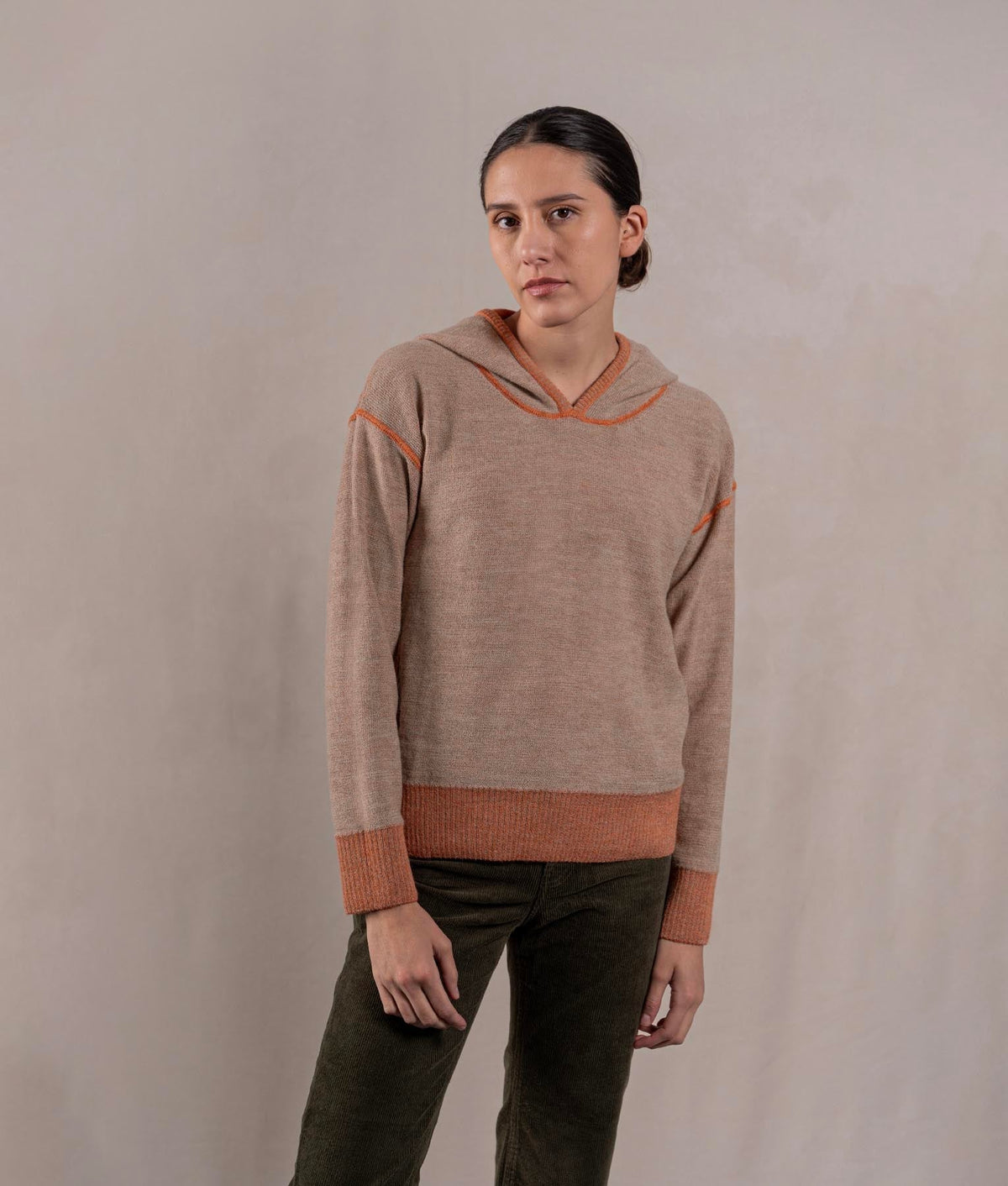 Woman wearing a taupe knit pullover hoodie with rust-orange contrast trim.