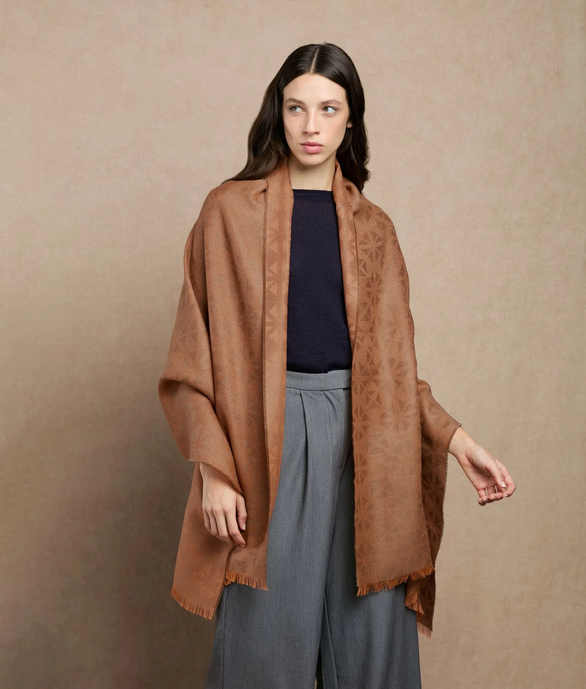 Woman wearing a brown textured shawl with fringe trim.